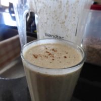 Tall glass of smoothie with cinnamon sprinkled on top, in front of a blender
